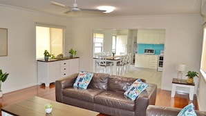 A modern living room with a leather sofa, a dining table, and a kitchen in the background. - Amble Inn - walk to the beach (SOUTH WEST ROCKS)