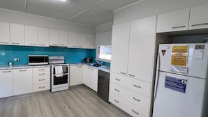 A modern kitchen with white cabinets, a microwave, an oven, a dishwasher, and a refrigerator with a note on it. - Amble Inn - walk to the beach (SOUTH WEST ROCKS)