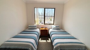 A small, single-room accommodation with two single beds, a nightstand, and a window providing a view of the street.