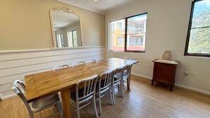 A dining room with a wooden table and chairs, a mirror, and a window with a view of buildings.