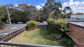 A fenced outdoor area with a grassy lawn, dense shrubbery, and a brick wall.