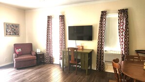 A living room with a wooden floor, a red armchair, a television, and patterned curtains.