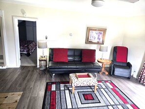 A living room with a black leather sofa, two side tables with lamps, a patterned rug, and a wheelchair.