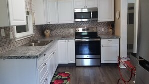 A compact kitchen with white cabinets, a stainless steel microwave, an oven, and a sink.
