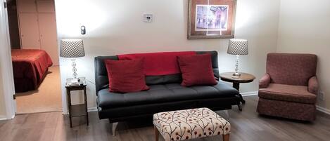A living room with a black sofa, red cushions, a patterned ottoman, a red armchair, and two side tables with lamps.
