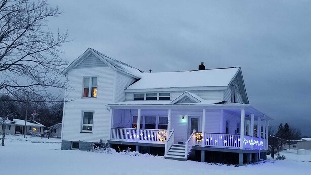 A two-story house with a covered porch, surrounded by snow.