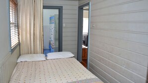 A narrow room with a bed, a window with blinds, and a door leading to another room. - Sunshine Cottage - walk to the beach - Bring your own linen (SOUTH WEST ROCKS)