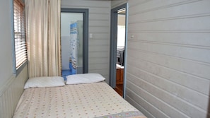 Cozy retreat with a single bed, featuring a quilted cover and two pillows, and a functional design with a window and door.