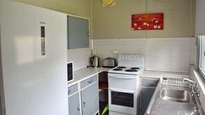 Compact kitchenette with a refrigerator, stove, toaster, and kettle, perfect for preparing meals on the go.