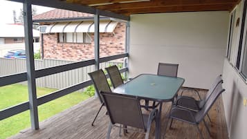 Relax in this outdoor space with a glass table and four chairs, surrounded by a wooden deck and metal railing.