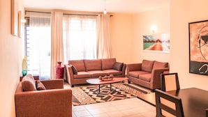 Ein Wohnzimmer mit zwei Sofas, einem Couchtisch und einem Teppich. An der Wand hängt ein Gemälde und es gibt ein Fenster mit Vorhängen.