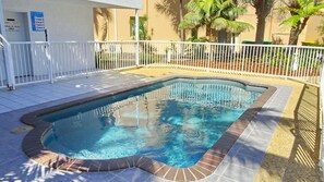 A swimming pool with a white fence and tiled deck.