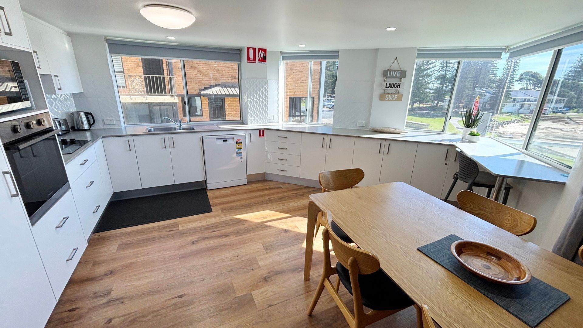 A modern kitchen with white cabinets, a wooden dining table, and a view of the outside.