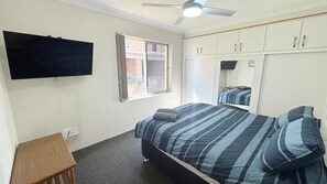 Un dormitorio con cama, televisor, ventana y ventilador de techo.