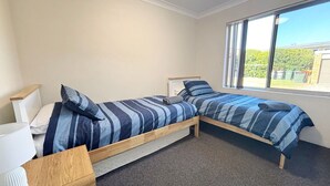 A bedroom with two single beds, a window, and a small bedside table. - Pacific Court 2 - walk to the beach - Linen supplied (SOUTH WEST ROCKS)
