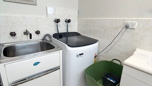 A compact kitchen with a stainless steel sink, a white dishwasher, and a green trash bin. - Pacific Court 2 - walk to the beach - Linen supplied (SOUTH WEST ROCKS)