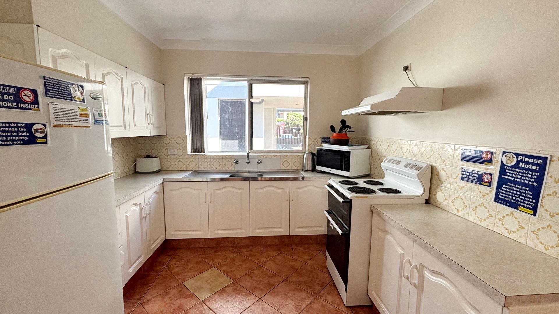 A compact kitchen with white cabinets, a stove, a microwave, and a toaster. There are signs on the walls, and a window with curtains.