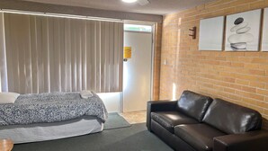 Une chambre d’hôtel avec un lit, un canapé en cuir, un mur en briques et une porte avec une pancarte.