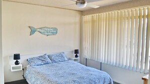 Une chambre à coucher avec un lit, deux lampes de chevet, un ventilateur de plafond et une fenêtre avec des stores.