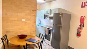 Une cuisine compacte avec un mur en briques, une table à manger avec des chaises, un réfrigérateur, un four à micro-ondes et une cuisinière.