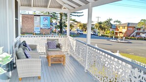 A covered outdoor seating area with wicker furniture and a wooden table. - Joanna Cottage - walk to the beach (SOUTH WEST ROCKS)
