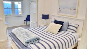 A bedroom with a striped bedspread, a bedside lamp, and a framed picture on the wall. - Joanna Cottage - walk to the beach (SOUTH WEST ROCKS)