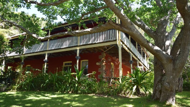 A two-story house with a balcony, surrounded by lush greenery.