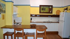 A compact kitchen with a wooden table and chairs, a stove, a sink, and a refrigerator.