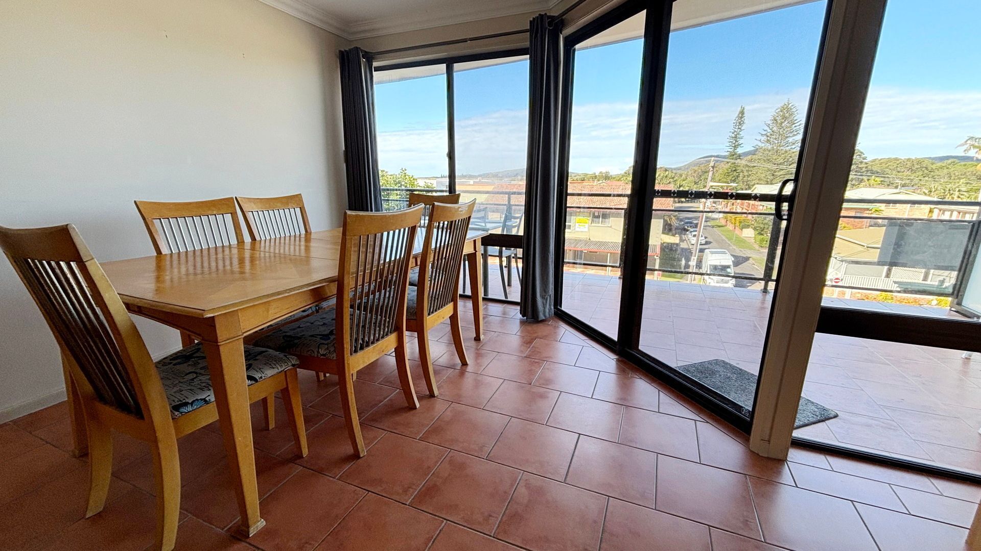 A dining area with a wooden table and chairs, large windows with a view of a residential area.