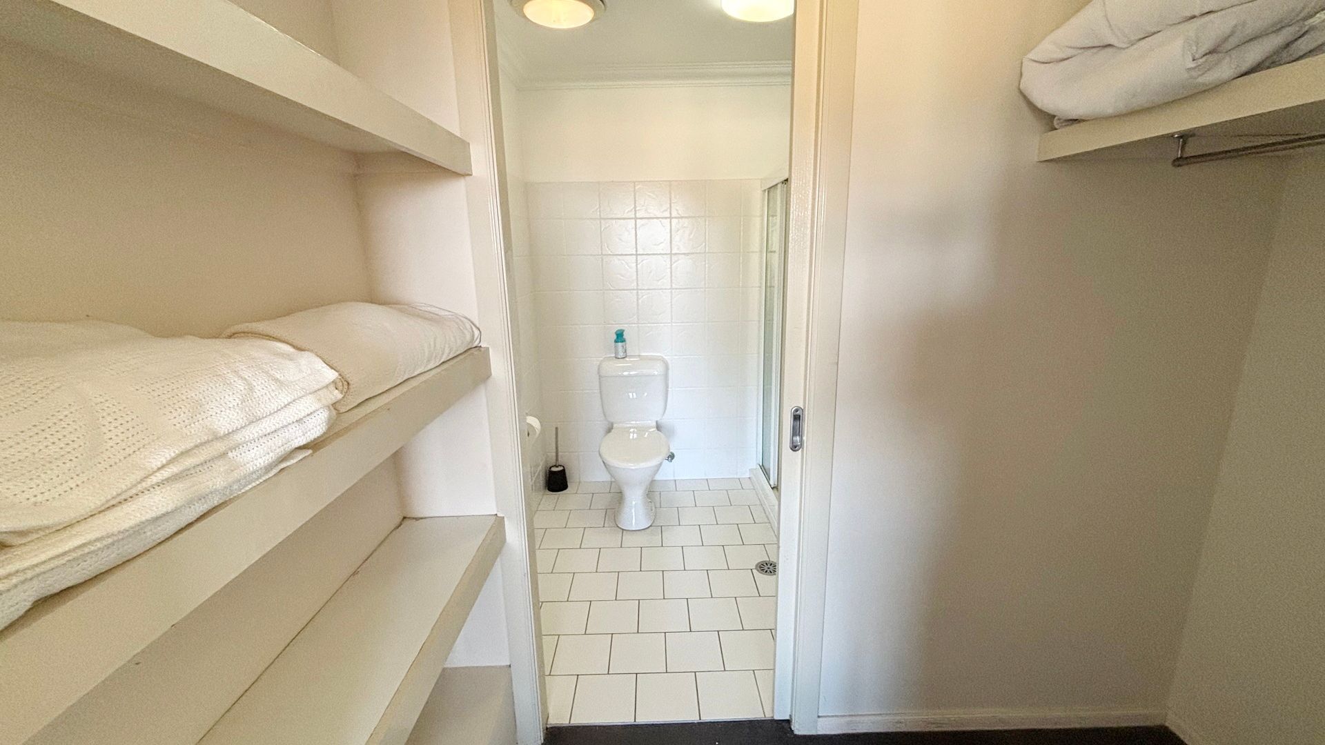 A narrow hallway leading to a bathroom with a toilet and a shower area.