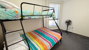 A bunk bed with a colorful striped mattress, a plain pillow, and a window with blinds.