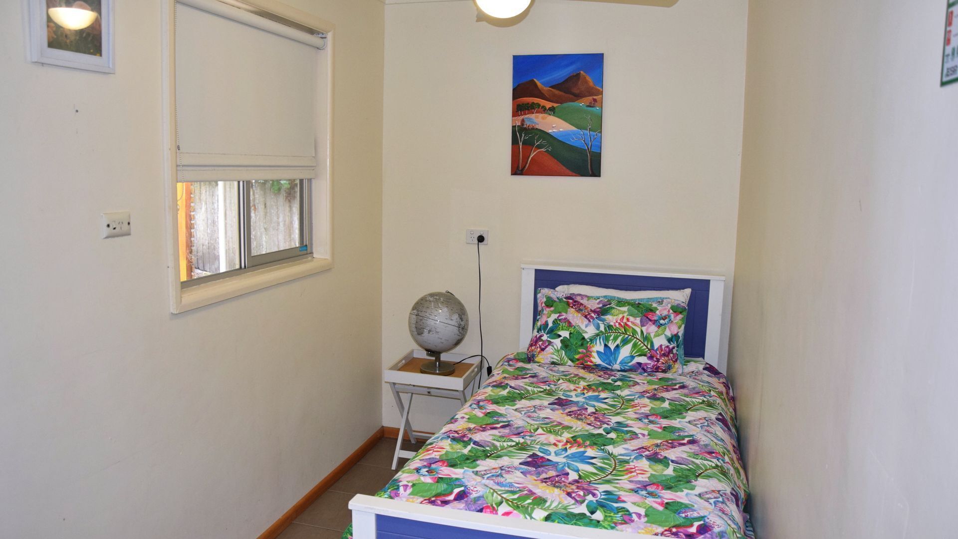 A small, neatly arranged bedroom with a bed, a globe on a side table, and a painting on the wall.