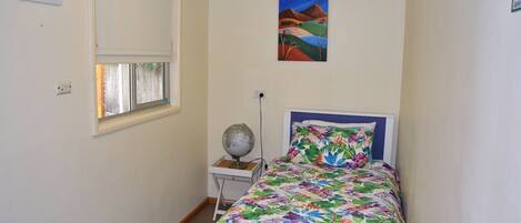 A small, neatly arranged bedroom with a bed, a globe on a side table, and a painting on the wall.
