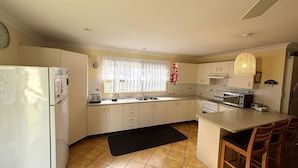 A compact kitchen with a refrigerator, stove, microwave, and a small dining area with chairs. - Wenlaw Cottage (Rear) Hat Head (HAT HEAD)