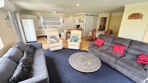 A living room with a grey sofa, a patterned armchair, two armchairs, a round coffee table, and a kitchen in the background. - Wenlaw Cottage (Rear) Hat Head (HAT HEAD)