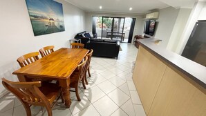 Un espace repas comprenant une table et des chaises en bois, un canapé noir et un coin cuisine avec un plan de travail et des placards.