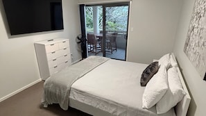 A bedroom with a bed, a dresser, a TV, and a sliding glass door leading to a balcony with chairs.