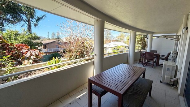 Un balcon avec une table et un banc en bois, une petite table avec des chaises, et une vue sur des maisons et des arbres.