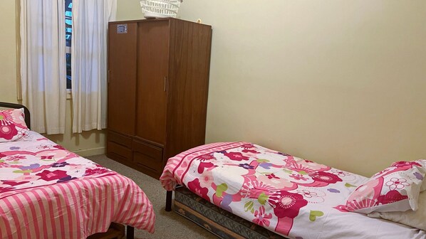 A bedroom with two single beds, a wooden wardrobe, and a window with curtains.