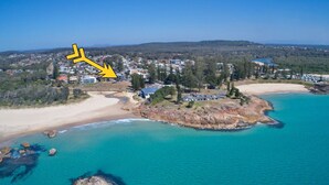 An aerial view of a coastal area with a beach, clear turquoise waters, and a town in the background. - Waterford Apartment 4 (SOUTH WEST ROCKS)