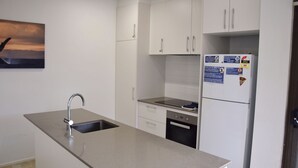 A modern kitchen with white cabinets, a stainless steel sink, and a built-in dishwasher. - Waterford Apartment 4 (SOUTH WEST ROCKS)