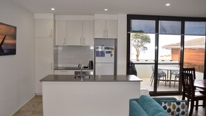A modern kitchen with white cabinets, a central island, and a dining area with a table and chairs. - Waterford Apartment 4 (SOUTH WEST ROCKS)