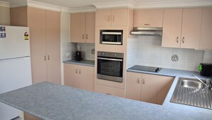 A kitchen with light pink cabinets, a stainless steel refrigerator, a microwave, an oven, a coffee maker, and a sink. - Astor Apartment 2 - walk to the beach (SOUTH WEST ROCKS)