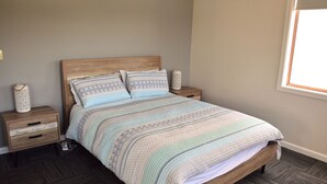 A bedroom with a wooden bed, a striped bedspread, two bedside tables with decorative vases, and a window with natural light. - Astor Apartment 2 - walk to the beach (SOUTH WEST ROCKS)
