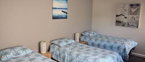 Una habitación con dos camas individuales, una mesita y un estante en la pared.
