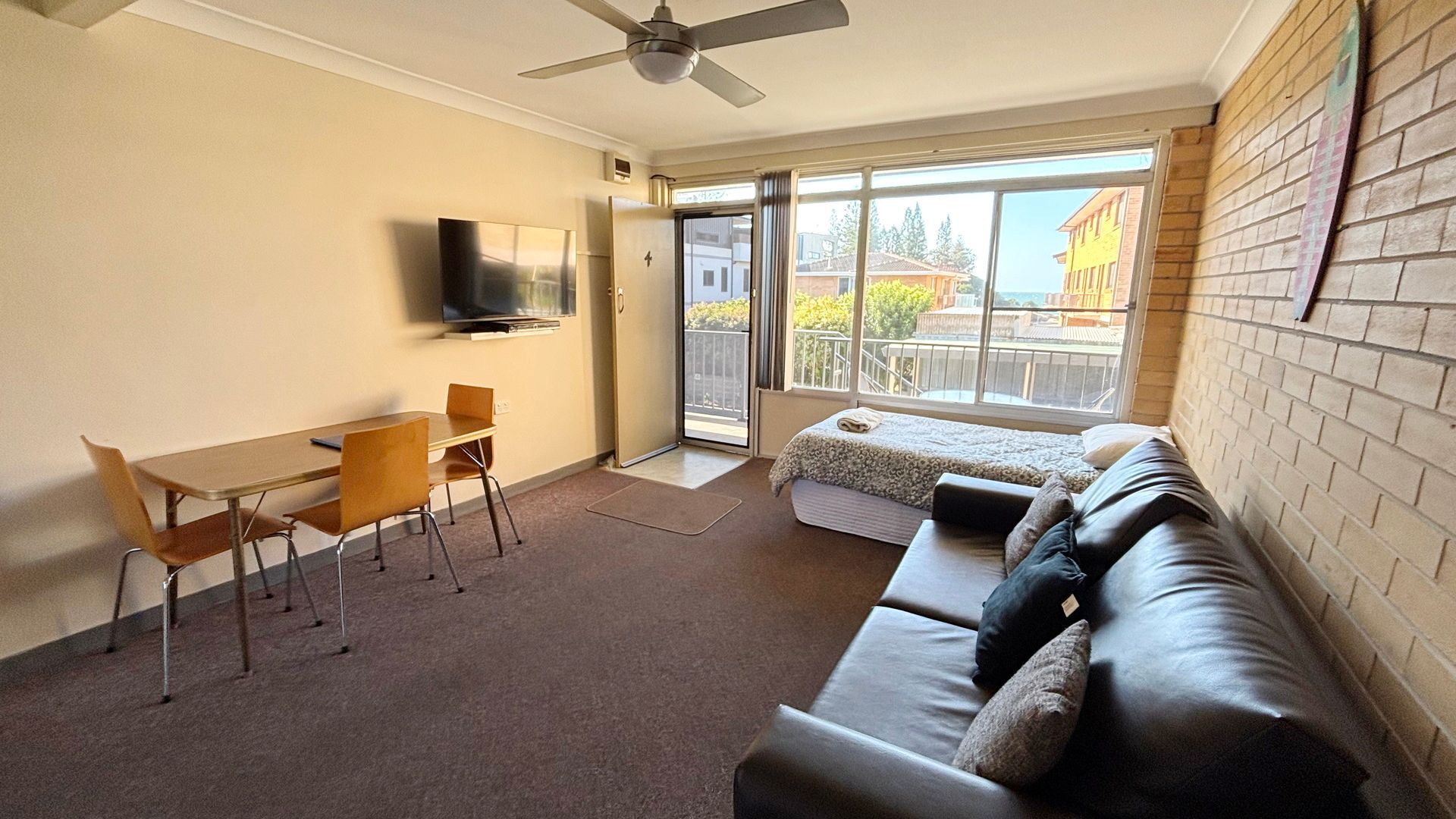 A room with a sofa, a TV, a dining table, and a balcony with a view.