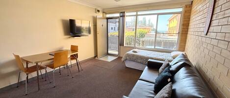 A room with a sofa, a TV, a dining table, and a balcony with a view.