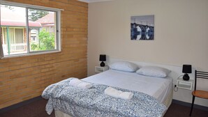 Een slaapkamer met een bed, twee nachtkastjes, een raam en een schilderij aan de muur.