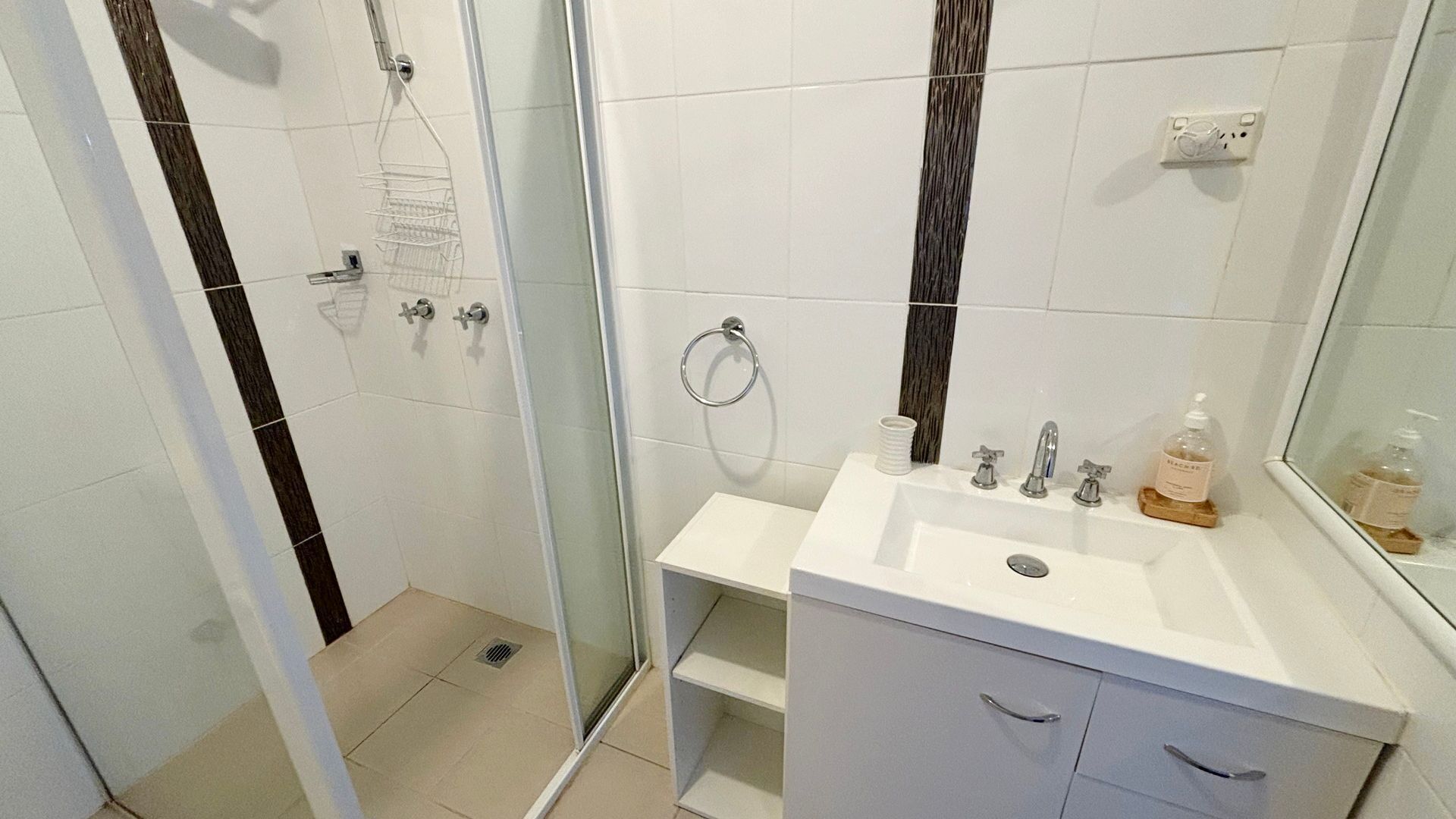 A bathroom with a glass shower enclosure, a white sink with a mirror, and a towel rack.