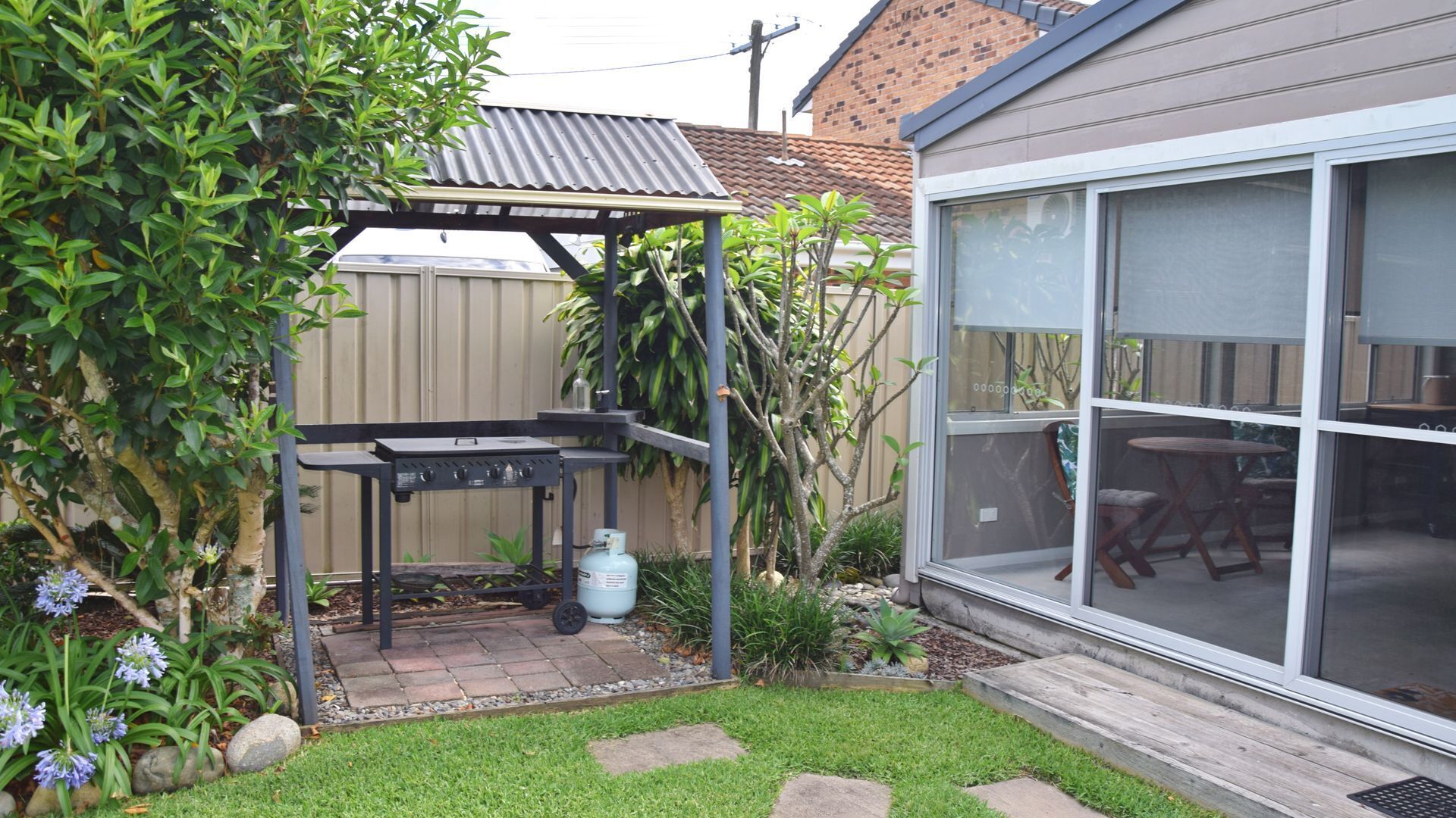 A backyard with a barbecue grill, a pergola, and a large window overlooking the yard.